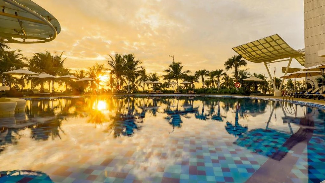 Tropical resort pool reflecting golden sunset with palm trees